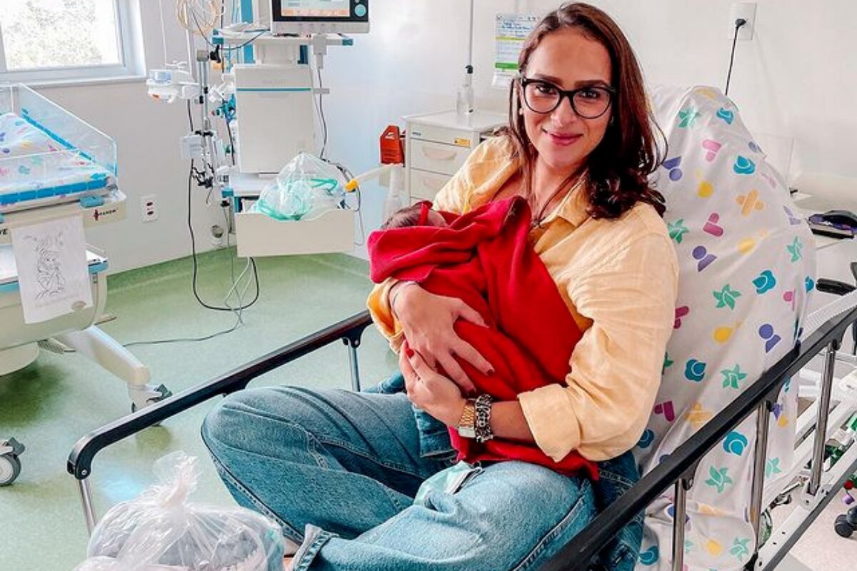 Letícia Cazarré com a filha. Maria Guilhermina, no colo, envolta numa manta vermelha, na cama do hospital