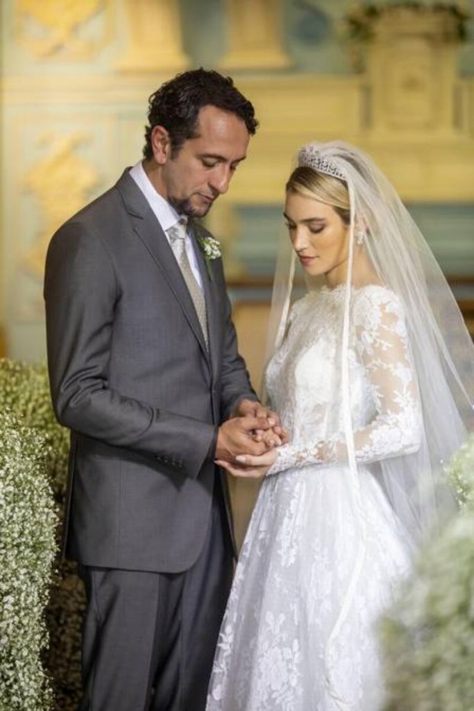 José Lucas (Irandhir Santos) e Erica (Marcela Fetter) de maos dadas, abençoando as alianças, no casamento, em 'Pantanal'