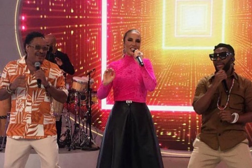 Cumpadre Washington dançando com Ivete sangalo, que está de saia preta e blusa rosa de manga comprida, e Beto Jamaica