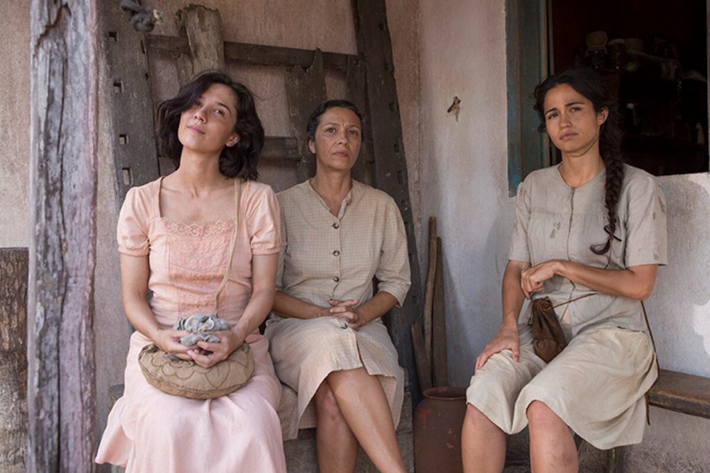 Marjorie Estiano, Cyria Coentro e Nanda Costa, sentadas, de saia e blusa nude, em cena do filme Entre Irmãs 