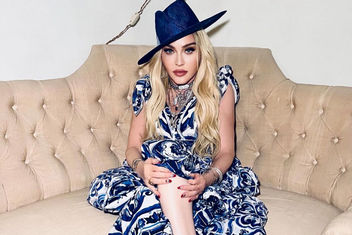 Madonna de vestido azul e branco, chapéu azul, sentada de pernas cruzadas