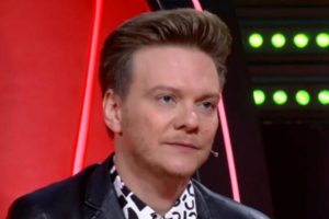 Michel Teló com expressão séria, sentado na cadeira do The Voice