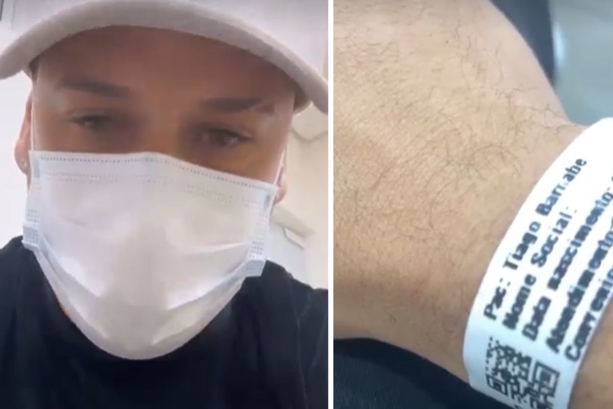 Tiago Barnabé de máscara, no hospital, mostrando a pulseira de atendimento