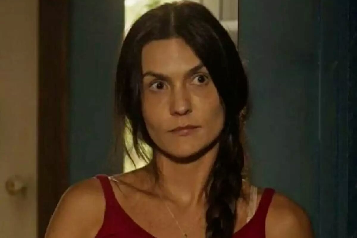Zefa (Paula Barbosa) de camiseta vermelha, cabelo preso, com trança pra frente do ombro