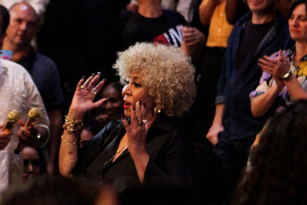 Alcione com os braços abertos na plateia do musical, de roupa preta