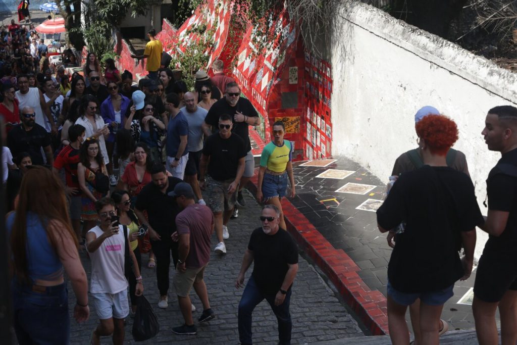 Dua Lipa com camisa verde e amarela, bermuda jeans, no meio da multidão, na escadaria Selaron, na Lapa, RJ e 