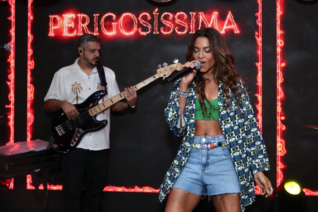 Lucy Alves de short jeans, cropped verde, blusãoo estampado verde e branco, cantando