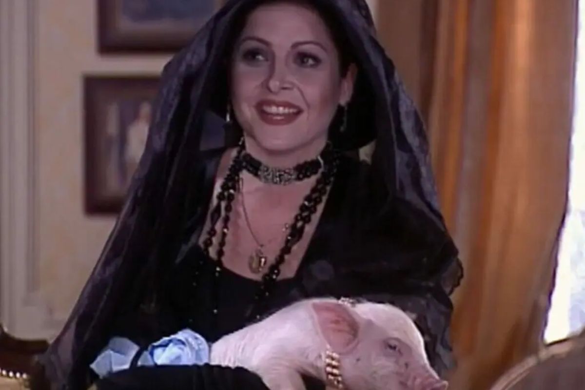 marcela (Drica Moraes), de roupa preta, com porquinha no colo