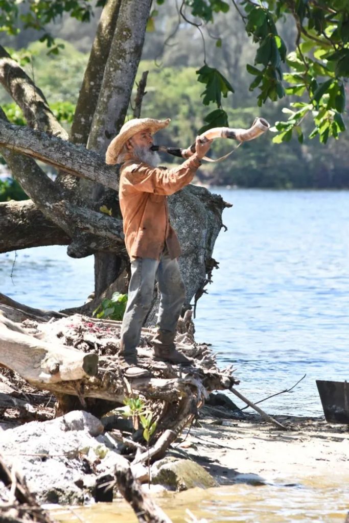 Velho do Rio (Osmar Prado) toca o berrante na beira do rio, em Pantanal