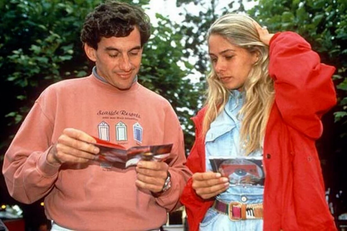 Ayrton Senna de moletom rosa e Adriane Galisteude casaco vermelho, ambos vendo uma revista