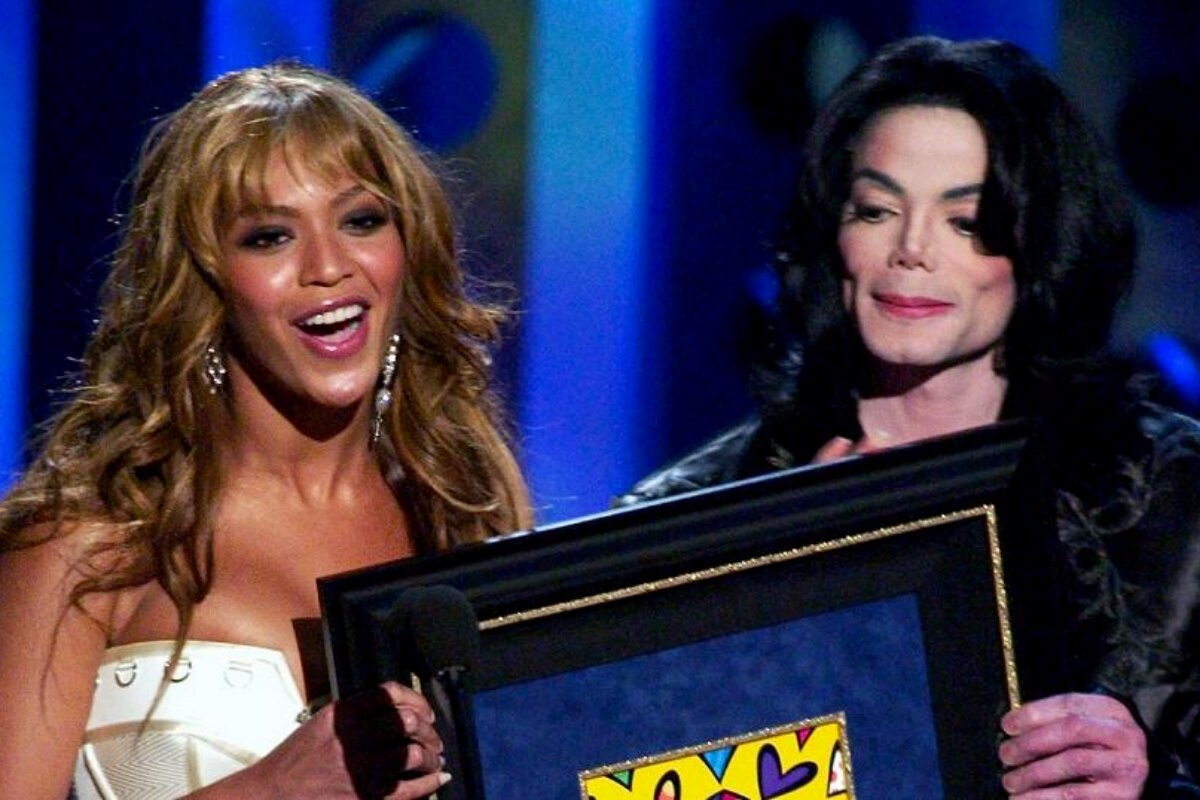 Beyoncé de tomara que caia branco e Michael Jackson, de preto, ambos segurando um quadro