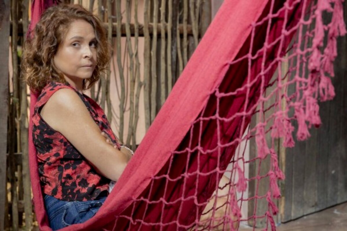 Drica Moraes, caracterizada como Núbia, de "Travessia", sentada numa rede vermelha