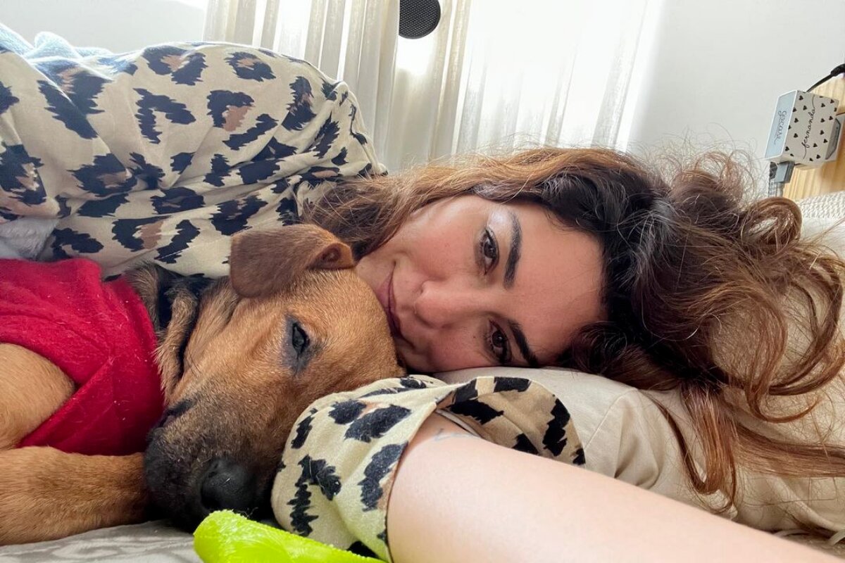 Fernanda Paes Leme deitada de casaco animal print, com a cachorra Matilda