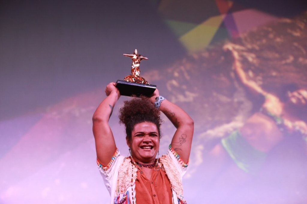 Kika Sena levantando o troféu, ce camisa laranja e outra branca