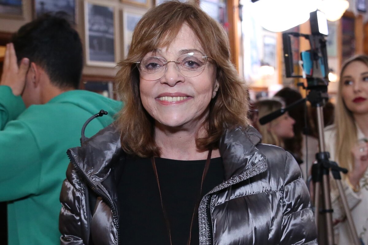Gloria Perez sorrindo, de jaqueta grafite e camisa preta, de óculos de grau
