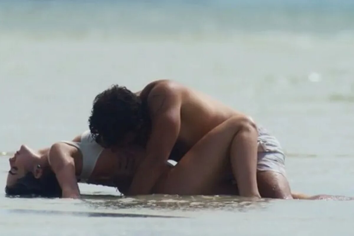 Chiara (Jade Picon) deitada no mar e Ari (Chay Suede) beijando-a, em "Travessia"