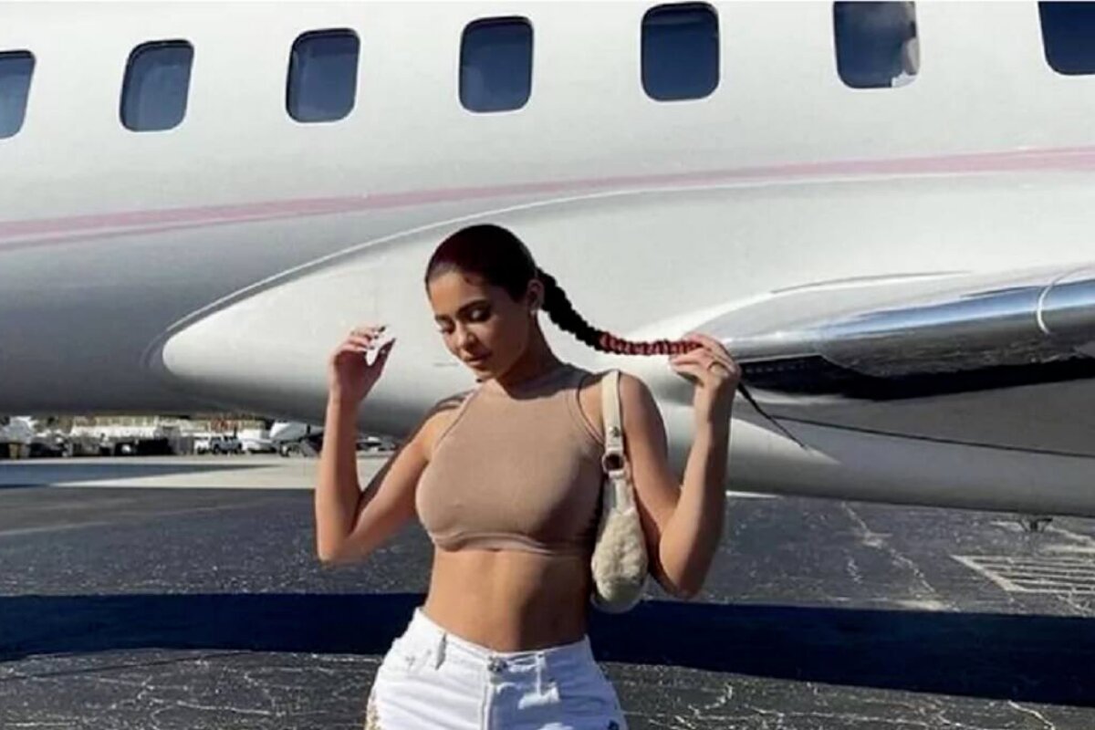 Kylie Jenner de cropped, barriga de fora e calça branca, diante de seu jatinho