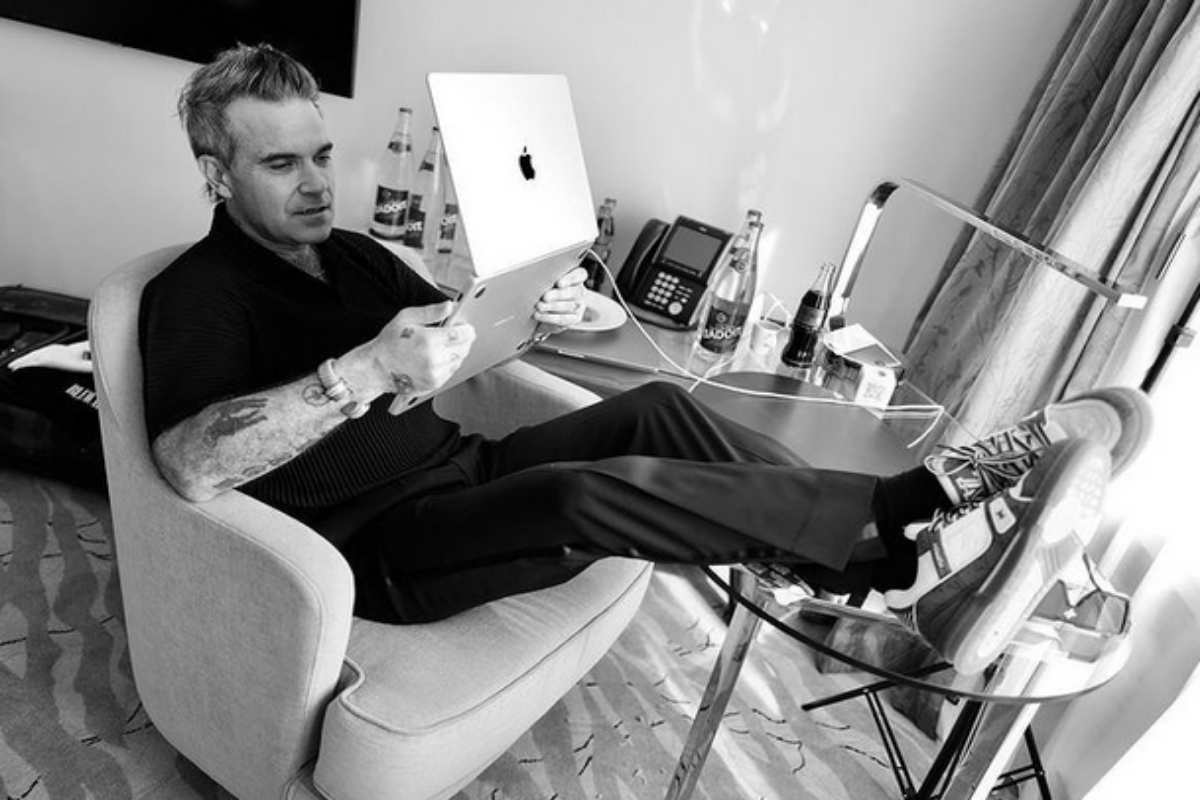 Robbie Williams sentado vendo o computador