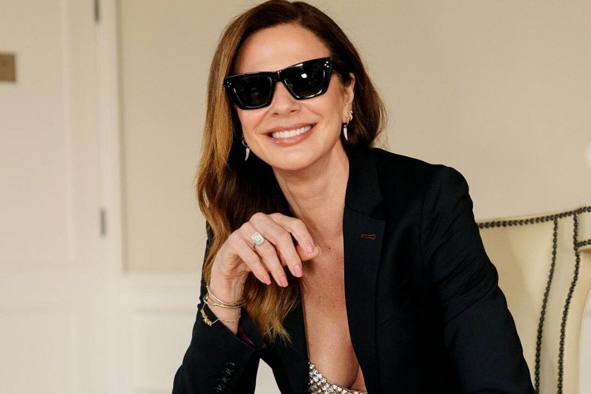 Luciana Gimenez de óculos preto e roupa preta, sentada, sorrindo