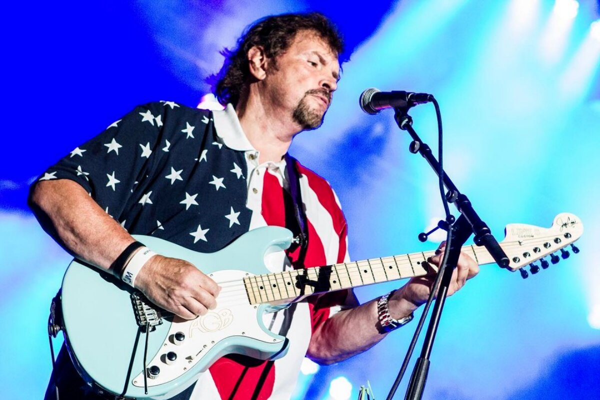 Jeff Cook de camisa com estampa da bandeira americana, tocando guitarra