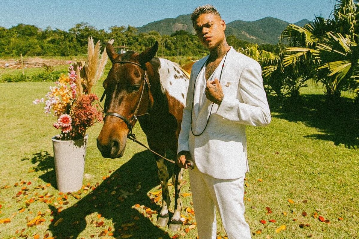 MC Cabelinho de branco, ao lado de um cavalo, num jardim