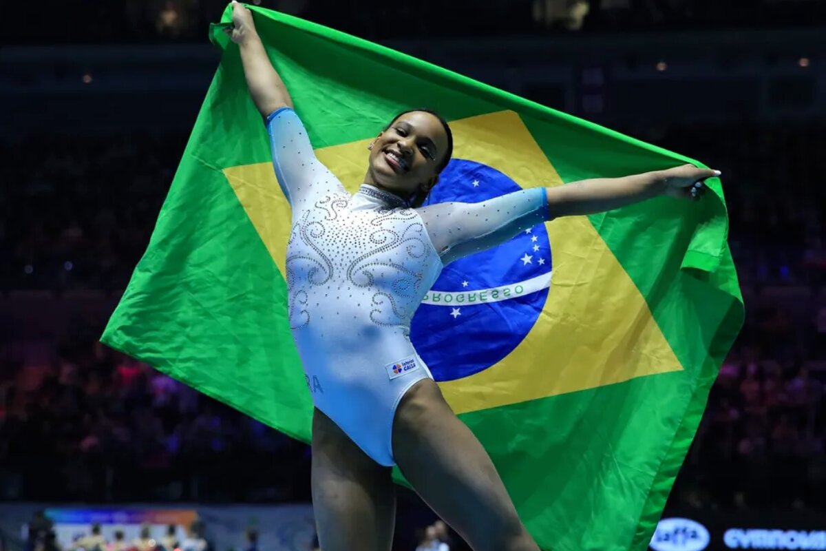 Rebeca Andrade com a bandeira do Brasil, de uniforme de ginasta