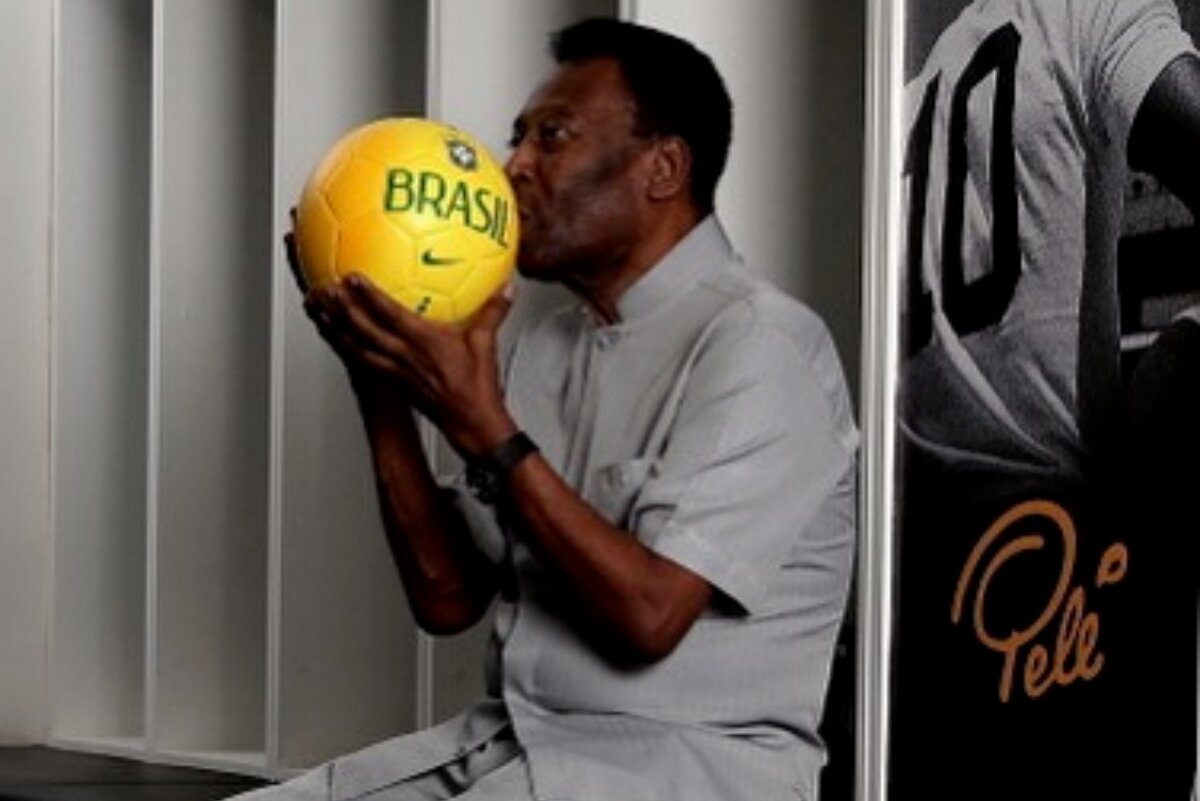 Pelé sentado no vestiário, beijando uma bola amarela, escrito 'Brasil'