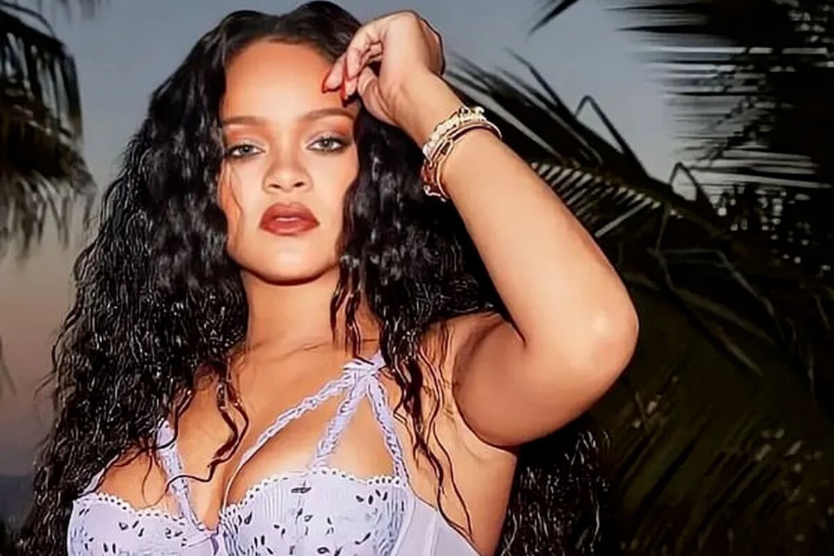 Rihanna de sutiã roxo, cabelos soltos, mão esquerda no cabelo