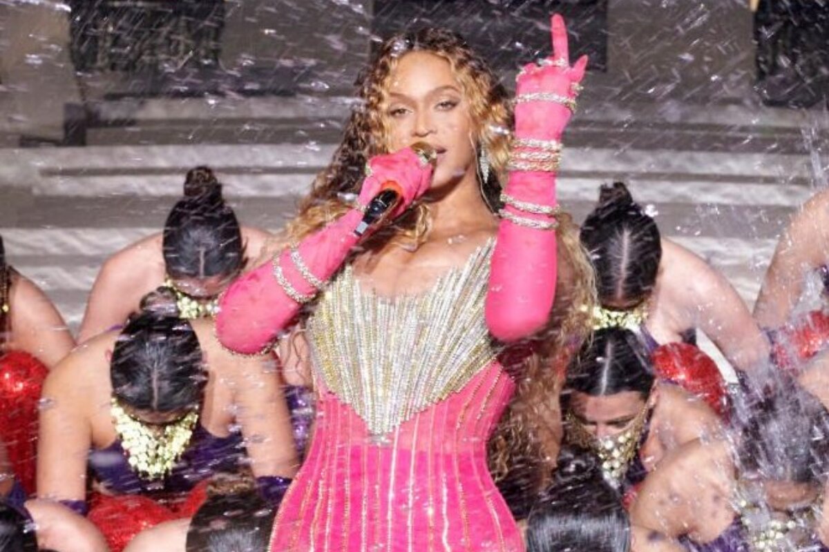 Beyoncé de vestido rosa com aplicações douradas, luva rosa, cantando, segurando microfone