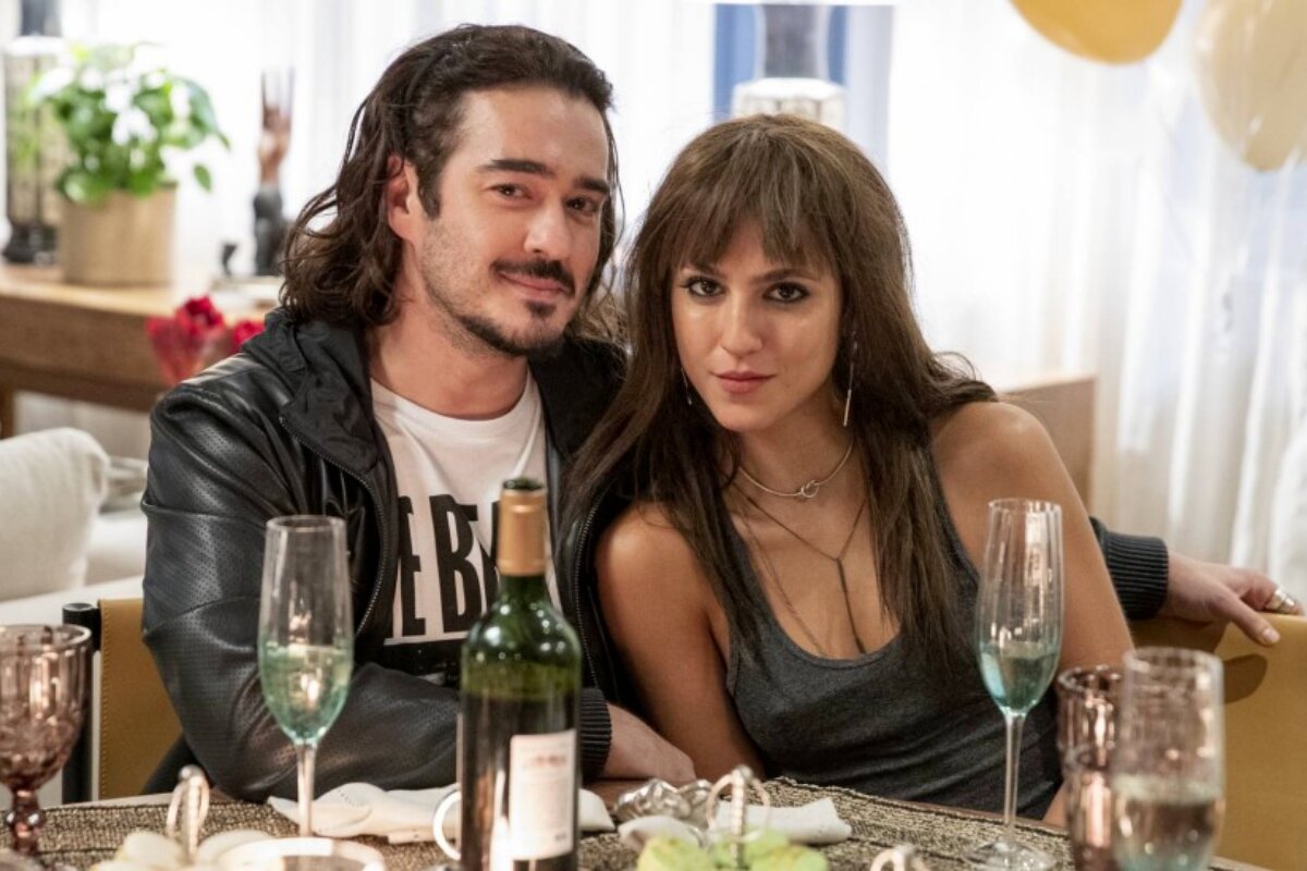 Marcos Veras e Flora Camolese sentados à mesa, abraçados, em cena de "Vai na Fé'