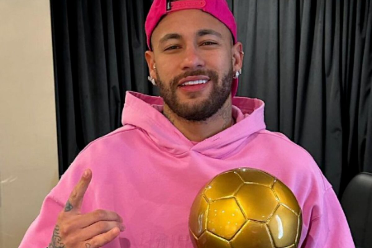 Neymar de casaco rosa segurando bola de ouro