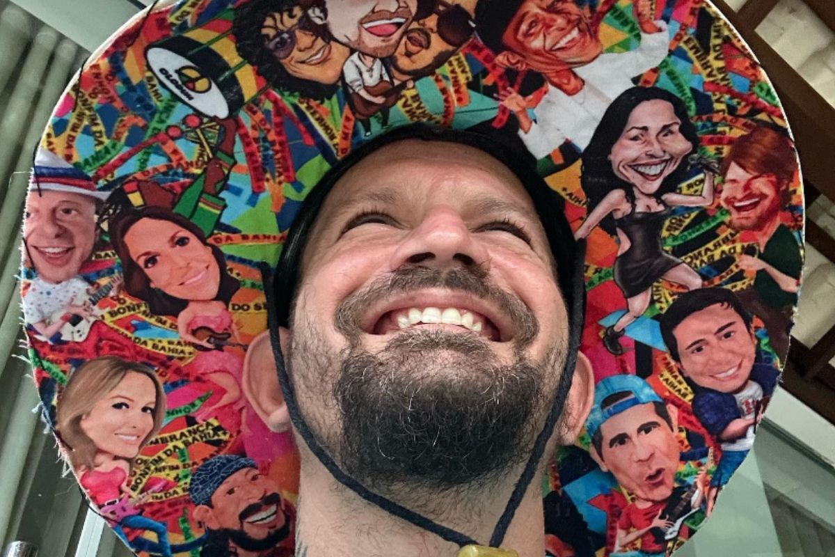 Saulo Fernandes, de chapéu colorido com imagens de cantores, sorridente
