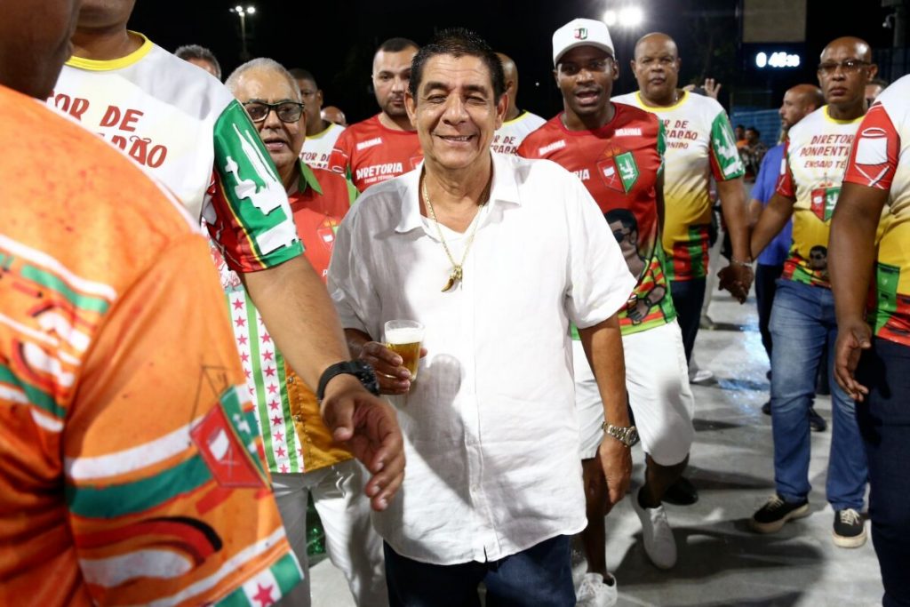 Zeca Pagodinho de camisa branca segurando copo de cerveja, no ensaio técnico da Grande Rio na Sapucaí 