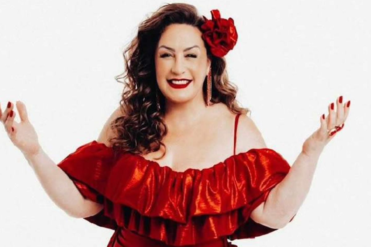 Gina Garcia, com os braços abertos, de vestido vermelho