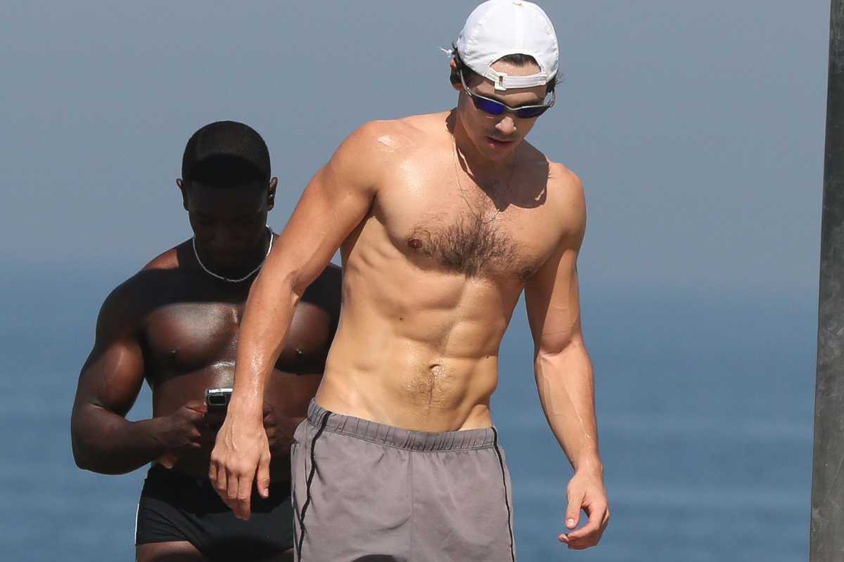 Nicolas Prattes sem camisa se exercitando na orla da praia