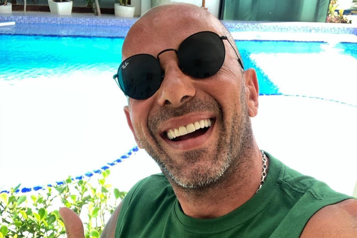 Rafael Ilha sorrindo, de óculos escuro e camisa verde