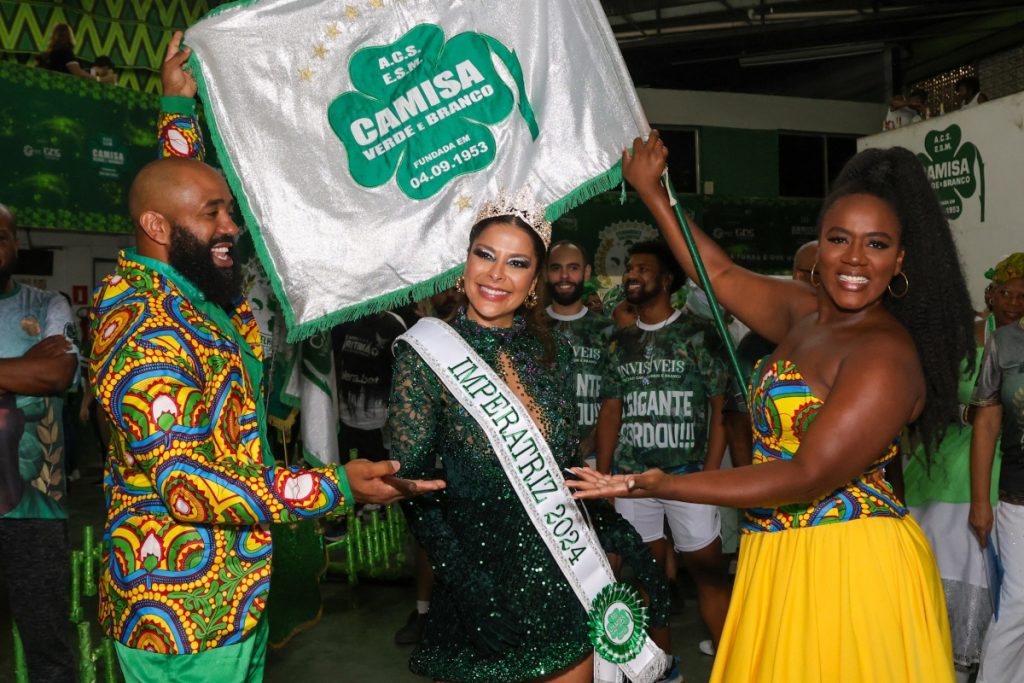 Gyselle Soares de coroa e vestido verde de brilhos entre o casal de mestre-sala e porta-bandeira