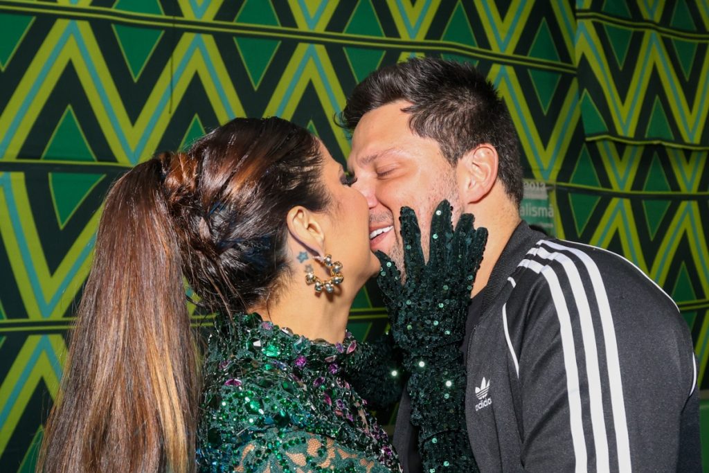 Gyselle Soares de coroa e vestido verde de brilhos beijando Thiago Servo