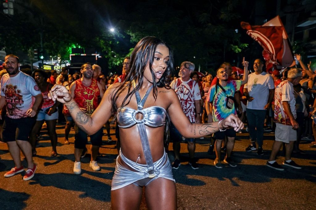 MC Rebecca de saia e top prata de recortes , com sandália gladiadora prata 