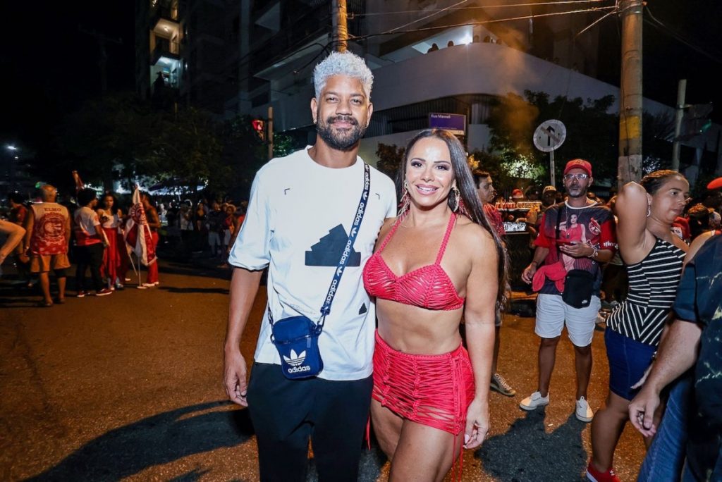 Viviane Araújo de short e  top vermelho ao lado do marido, de camisa branca e calça jeans