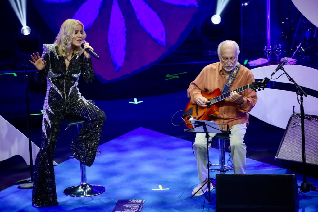Paula Toller e Roberto Menescal sentados cantando 
