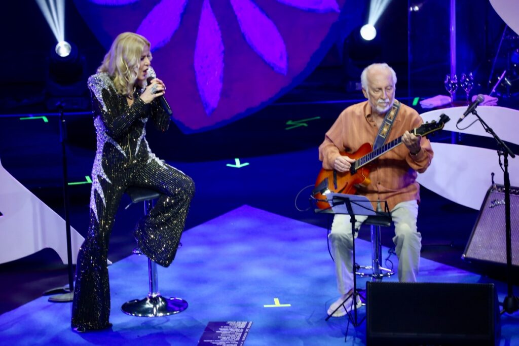 Paula Toller e Roberto Menescal sentados cantando 