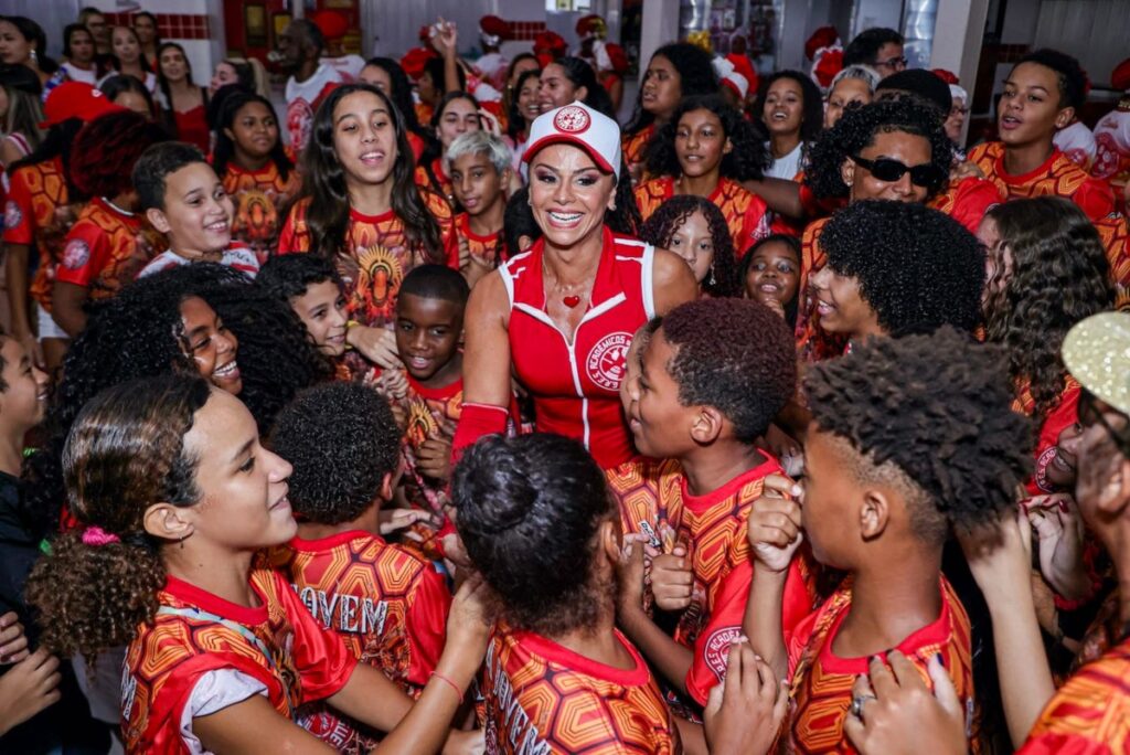 Viviane Araújo de macacquinho vermelho e branco, boné vermelho e branco, bota branca rodeada por crianças 