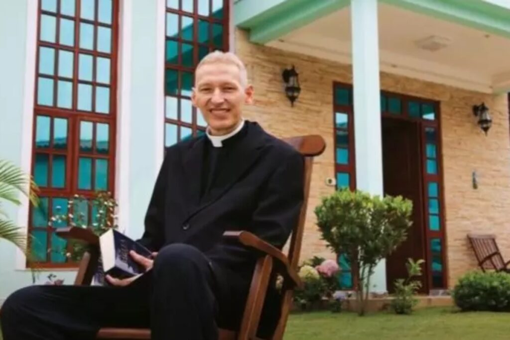 Padre Marcelo Rossi sentado numa cadeira, na fachada de casa, com a Bíblia na mão 