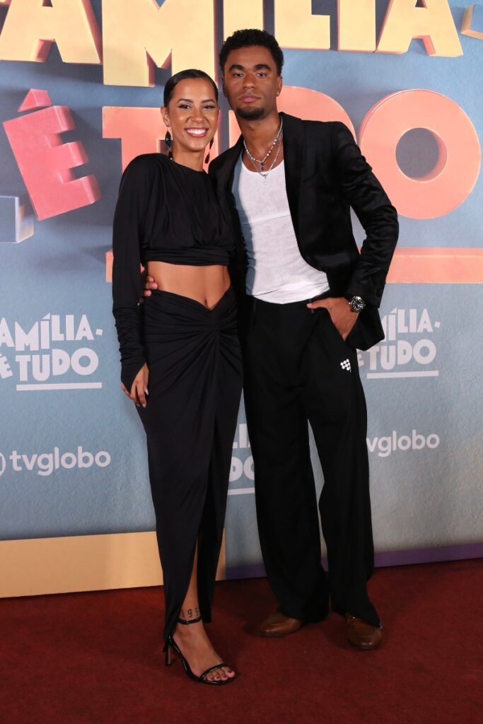 Ramille de vestido preto abraçada a Isacque Lopes, de blazer e calça prata, camisa branca , na festa de lançamento da novela Família é Tudo 