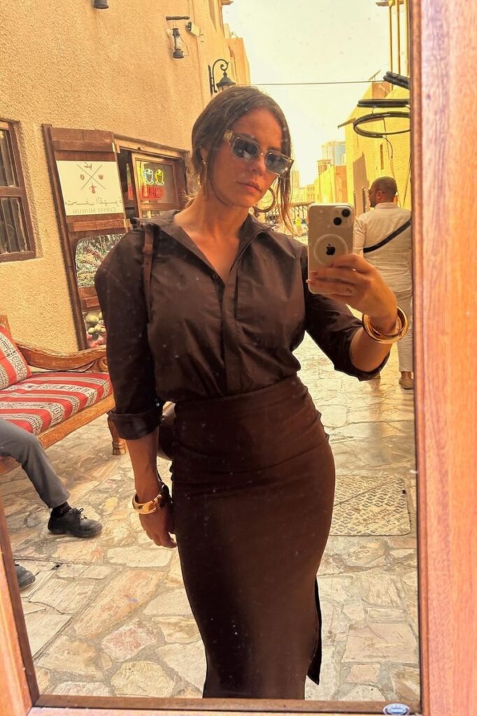 Paolla Oliveira de camisa marrom de manga longa e saia longa no mesmo tom, fazendo selfie  