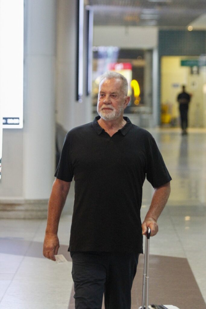 Luiz Fernando Guimarães de camisa preta e calça jeans, com mala, no aeroporto 