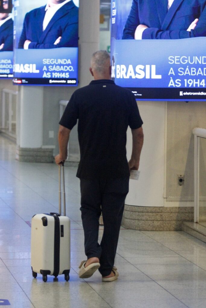 Luiz Fernando Guimarães de camisa preta e calça jeans, com mala, no aeroporto 