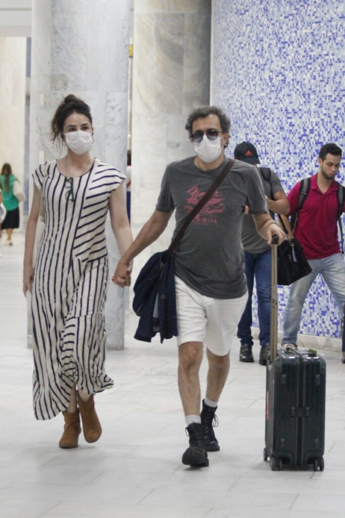 Larissa Bracher e Paulinho Moska de mãos dadas, com máscara de proteção,  no aeroporto