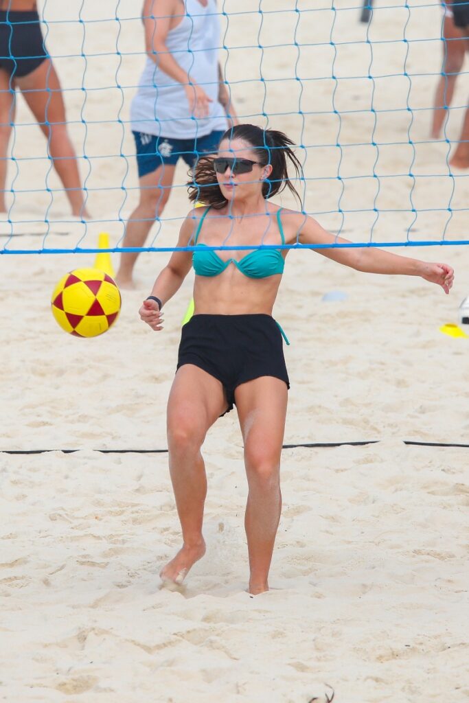 Jade Picon de biquíni azul e short preto jogando futvôlei na praia 